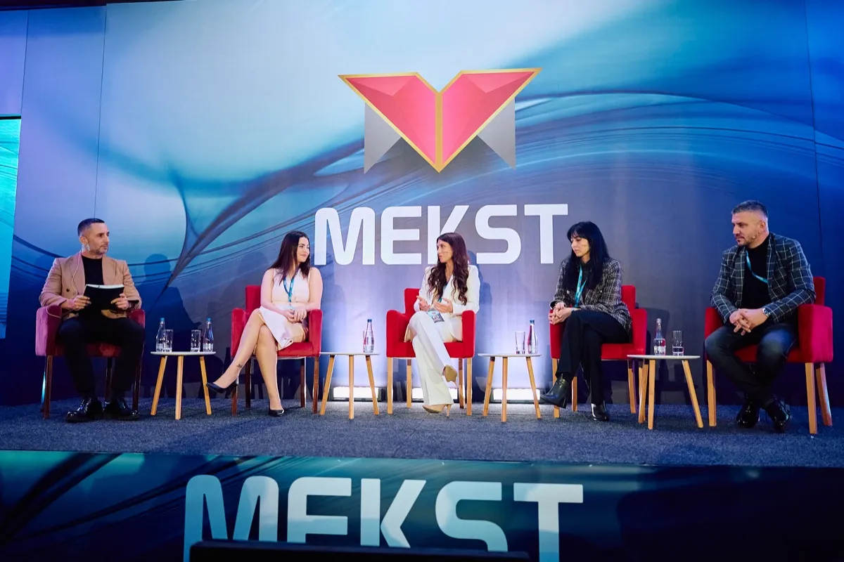 Panel diskusija na bini sa crvenim foteljama i belim stočićima